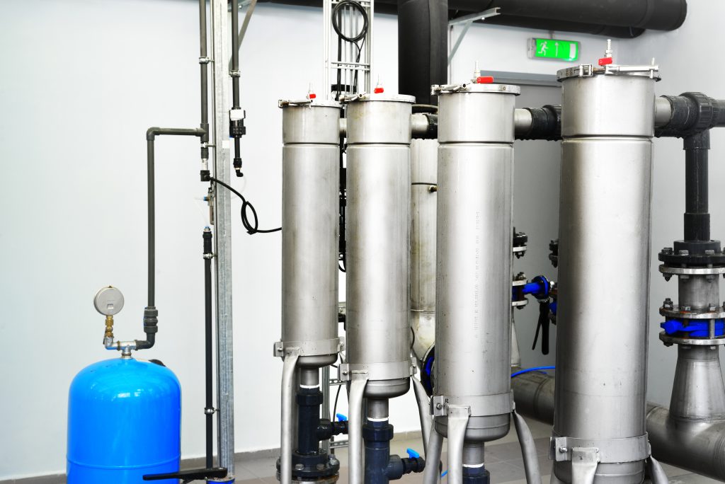 Large industrial water treatment and boiler room. Shiny steel metal pipes and blue pumps and valves.